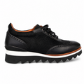 A black low-top platform shoe with a mix of smooth leather and textured suede-like panels, featuring black laces, a thick white midsole, and a black zigzag lug outsole, shown against a plain white background.