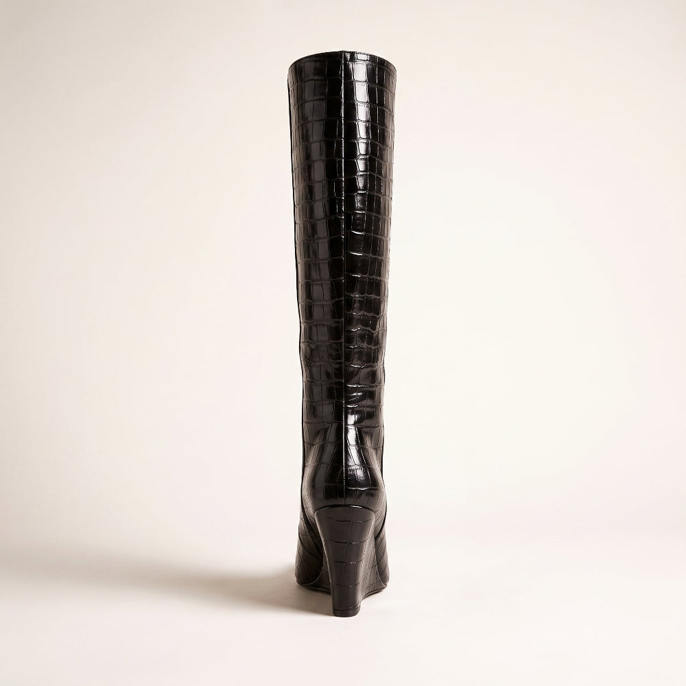 A single black knee-high boot with a glossy crocodile-embossed texture and a high stiletto heel, shown from the back against a plain off-white background.