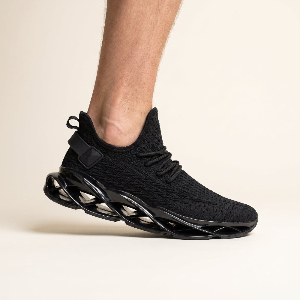 A black knit athletic sneaker with a sculpted black sole, shown worn on a person's foot against a clean off-white studio background.