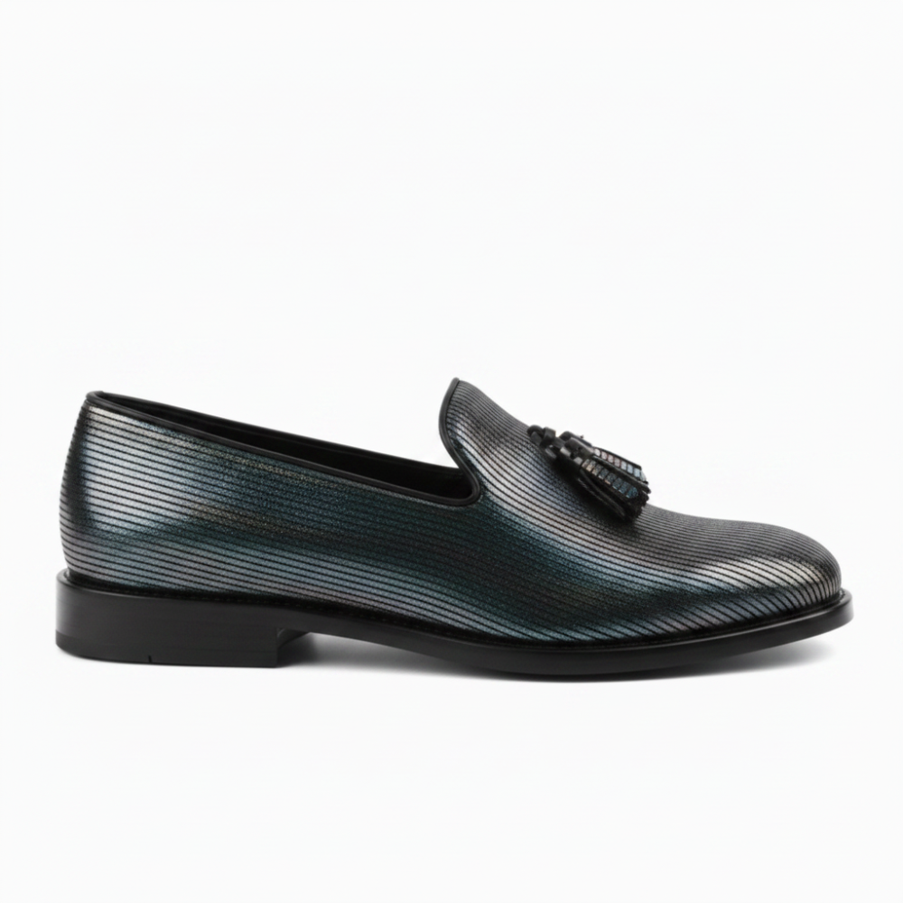 A single men's loafer in a textured, iridescent metallic finish that shifts between silver, blue, and green, featuring a black tassel detail on the strap and a black sole.