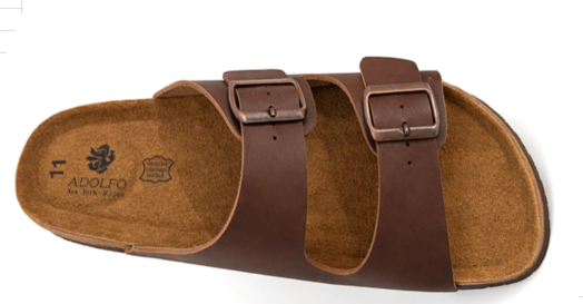 A single brown double-strap slide sandal with metal buckles, shown from a top-down angle on a white background. The brand name 'ADOLFO' is visible on the footbed.