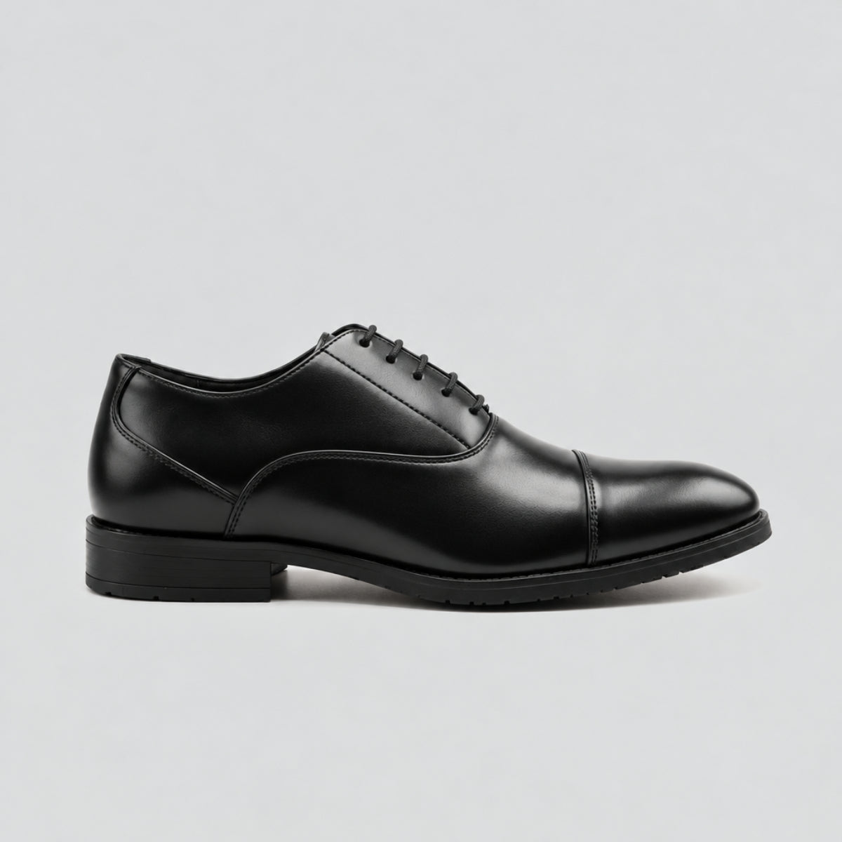 A single black  leather oxford dress shoe with a cap toe and dark sole, shown in a side profile on a light gray background.