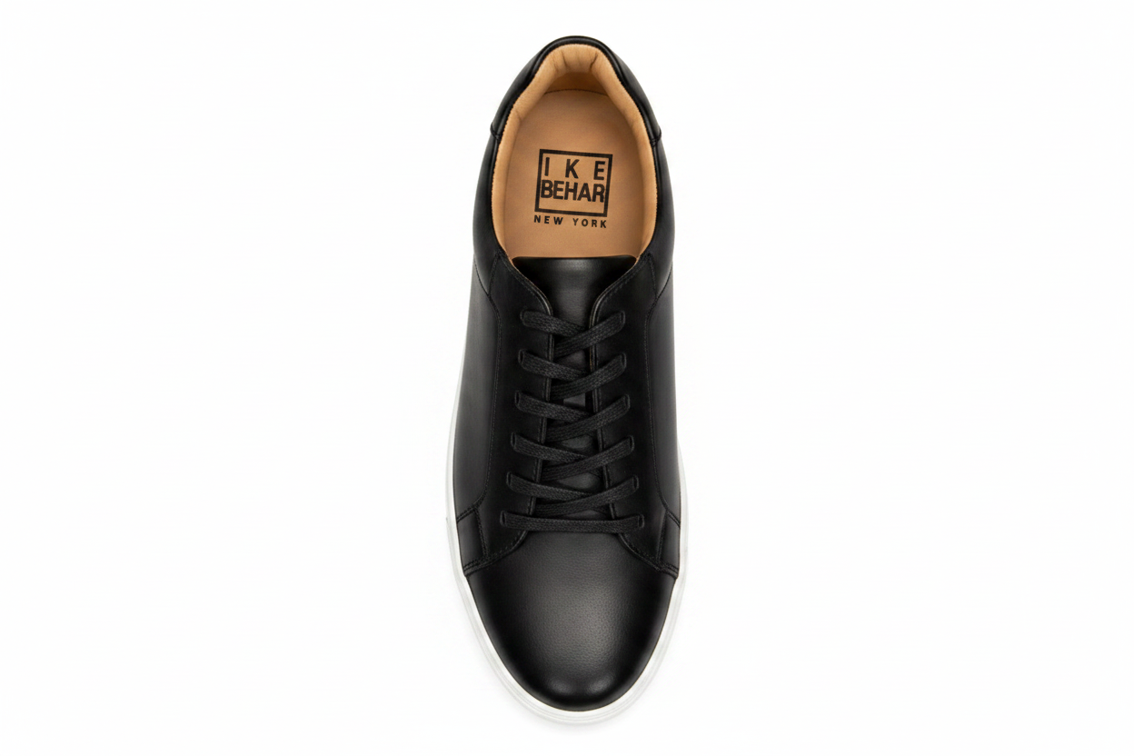 A top-down view of a black  leather sneaker by Ike Behar, featuring dark brown laces and a light beige outsole, set against a plain white background.